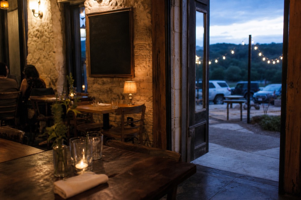 Interior of an old limestone-walled Texas restaurant with wooden tables, warm lamps and a chalk menu board without legible text
