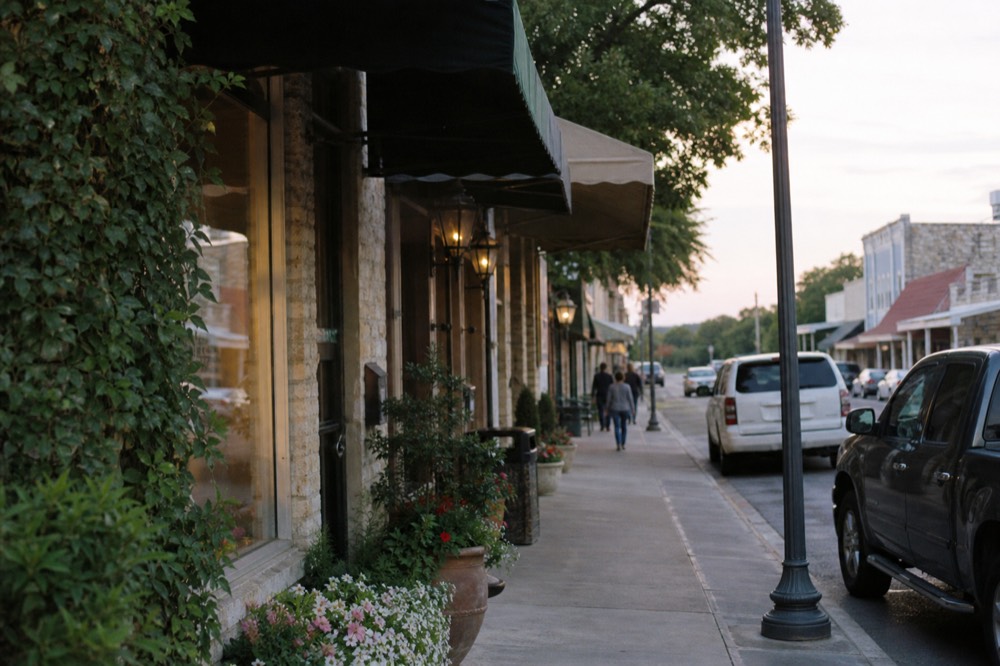 Main Street storefronts in a German-Texan town at golden hour with awnings, planters and parked cars