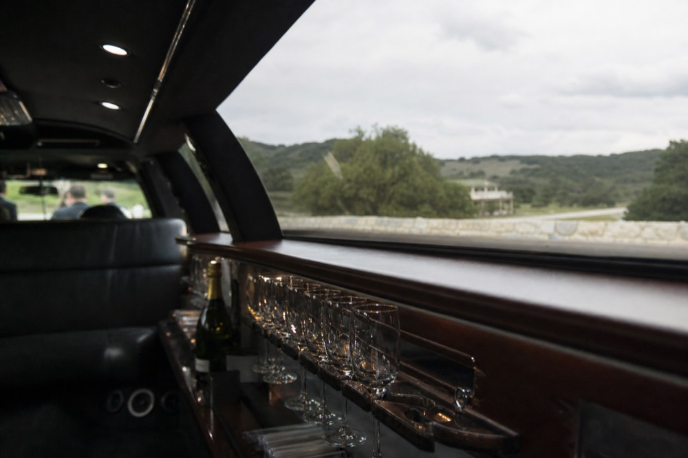 The interior of a stretched limousine with a row of empty wine glasses in a rack and a bottle secured in a holder, soft interior lighting
