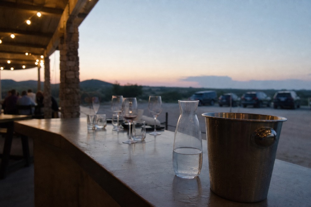 Stainless dump bucket and a water pitcher at the end of a winery tasting bar with used glasses beside them