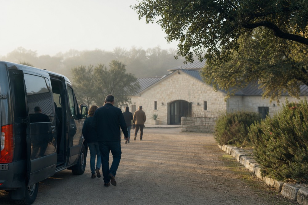Small group stepping down from a shuttle van onto a gravel drive in front of a limestone winery building