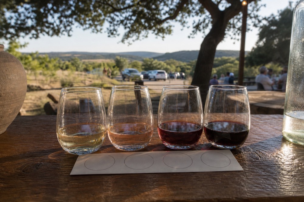Close-up of a small printed tasting flight card and four partly filled glasses on a wooden bar top, no visible branding