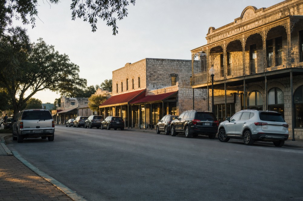 Historic limestone storefronts along a small Texas main street at golden hour with parked cars and shade trees