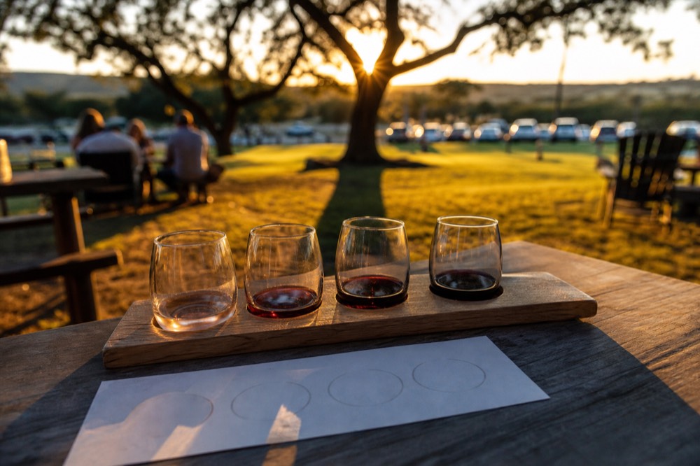 A flight of four small wine glasses on a wooden paddle beside a printed tasting card, shallow depth of field